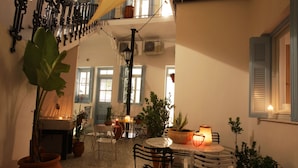 An indoor courtyard with a round table, chairs, potted plants, and hanging lights. - Live in Athens, Thiseio Historic House (Athens)