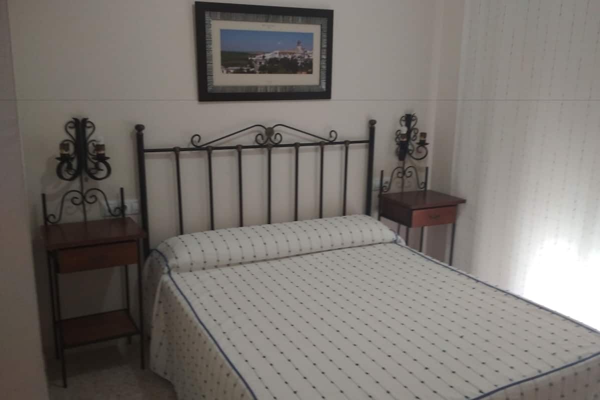 Ein Schlafzimmer mit Bett, Nachttisch, einem gerahmten Bild an der Wand und einem Fenster mit Jalousien.