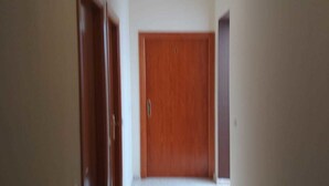 Un pasillo estrecho con una puerta de madera al final, una lámpara en el techo y suelo alfombrado.