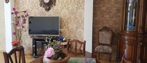 A dining area with a table, chairs, a potted plant, a television, and a cabinet.