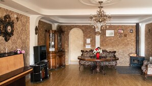 A spacious living room with a wooden floor, a large wooden cabinet, a television, a chandelier, and a stone wall. - Hilltop Mestia (Mestia)
