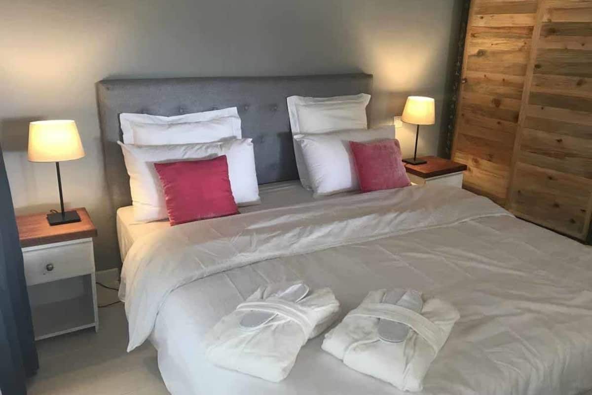 A neatly made bed with white bedding and two pillows, one red and one white, in a room with wooden paneling on the wall.