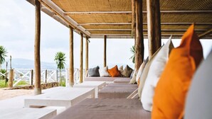 Un espace extérieur abrité, doté de bancs et de coussins blancs, offrant une vue sur un paysage pittoresque.