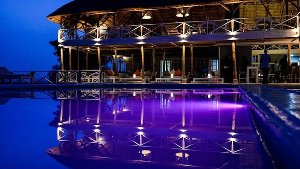 Un immeuble à plusieurs niveaux doté d’une piscine dont l’eau reflète les lumières, d’un espace extérieur couvert avec des sièges et d’une vue sur l’eau.