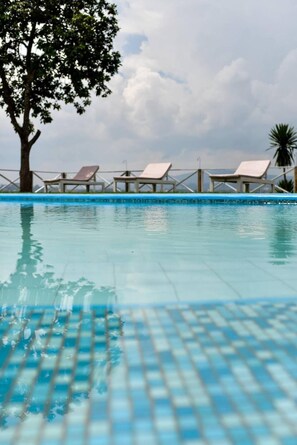 A swimming pool with lounge chairs and a tree.