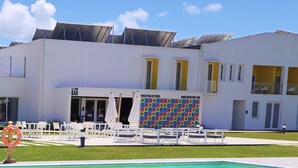 Una piscina con un jacuzzi en primer plano, un edificio blanco con detalles amarillos al fondo y una pared colorida con varios iconos.