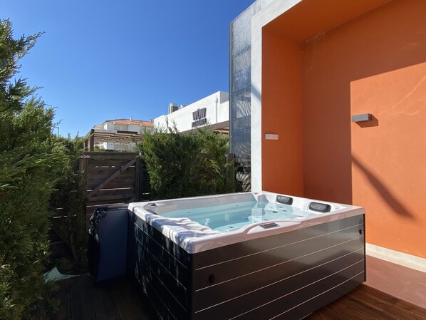 A hot tub in a backyard with a wooden fence and a building in the background.