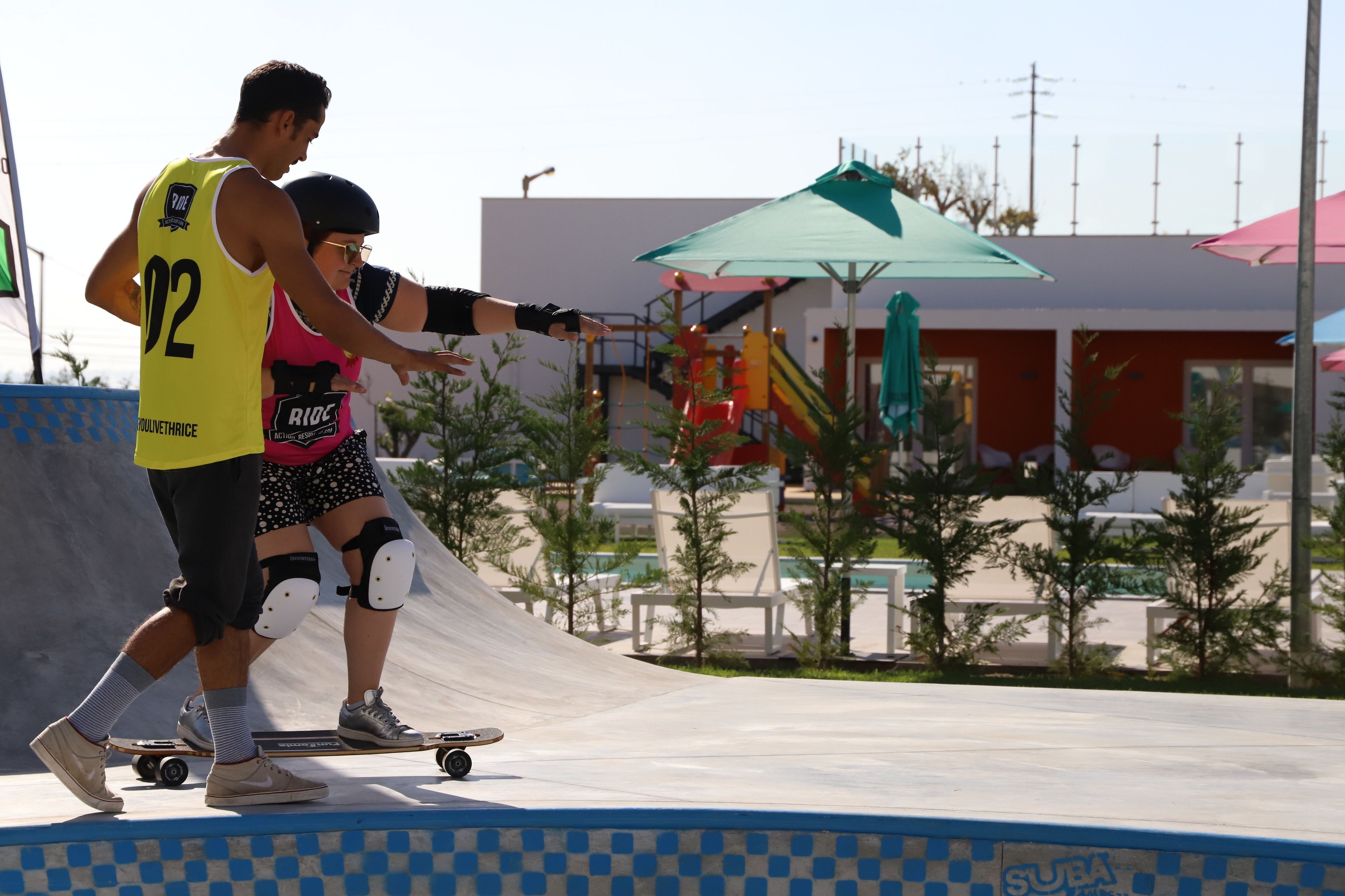 A person skateboarding at a skate park with a ramp and various structures in the background.