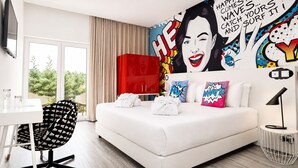 Habitación de hotel moderna con una cama grande, un escritorio, una silla y vistas a la vegetación.