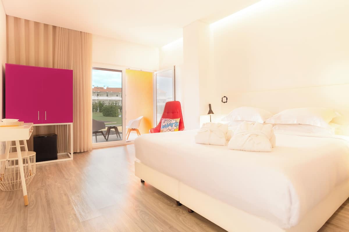 A hotel room with a large bed, a desk, a chair, and a view of the outdoors.