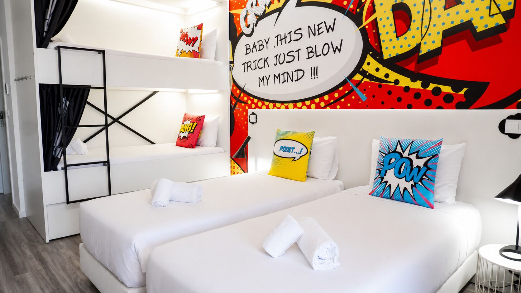 Habitación de hotel con dos camas, una litera y un llamativo mural de estilo cómic.
