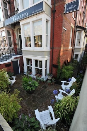 A building labeled 'THE GALLERY' with a brick facade, white windows, and a small garden area with potted plants and white chairs. - The Gallery (Blackpool)