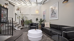 A modern living room with a black leather sofa, a white round coffee table, and a staircase leading to an upper level. - Stephansens Hotel (Randers)
