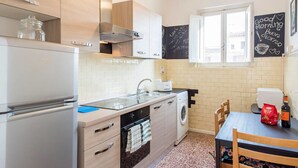 Cocina compacta con refrigerador, estufa, lavaplatos y lavadora. Hay una pizarra con escritura en la pared y una ventana con vista a edificios.