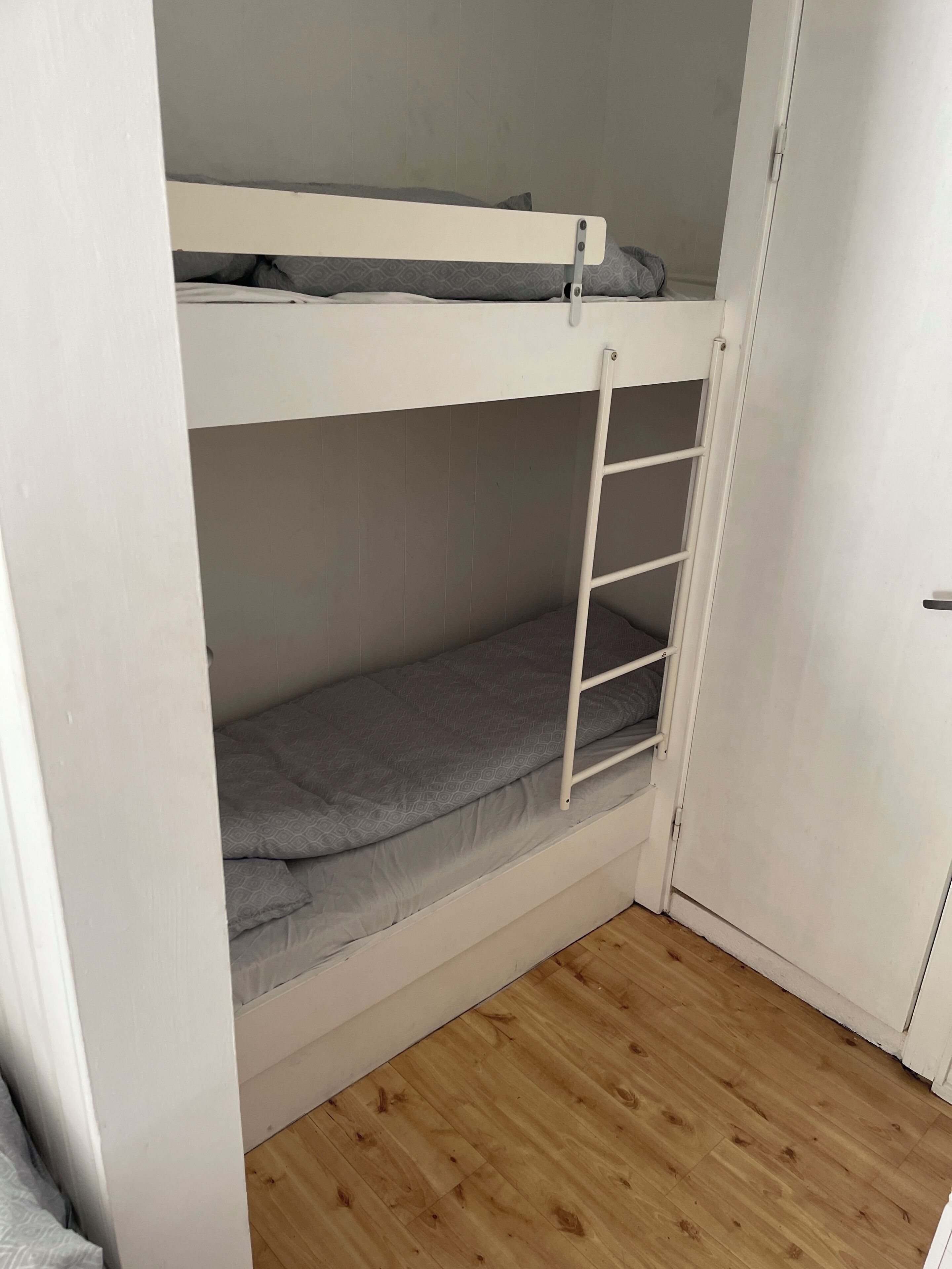 A bunk bed with a ladder, a wooden floor, and a white door.