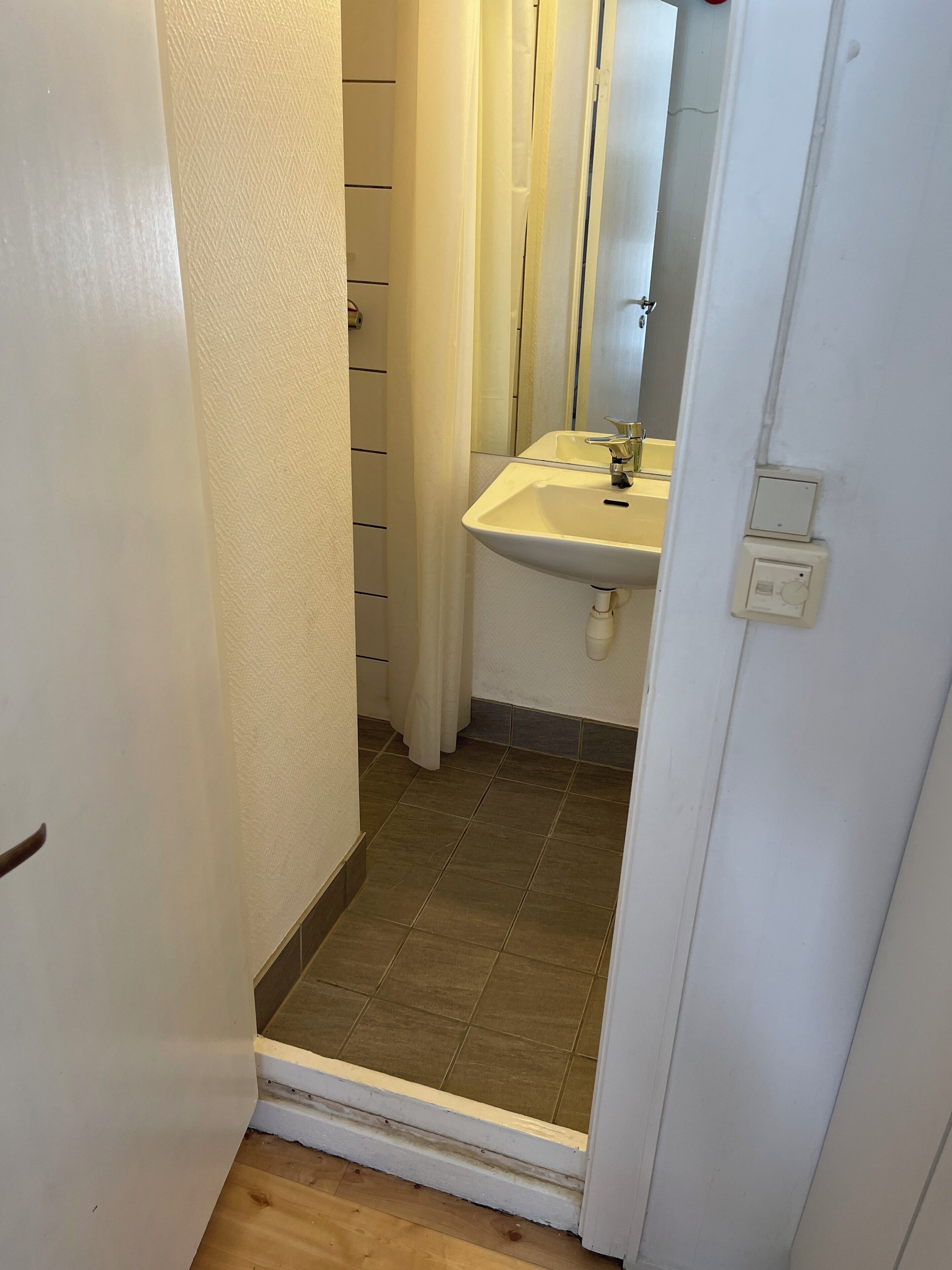 A narrow hallway with a bathroom featuring a sink, mirror, and tiled floor.