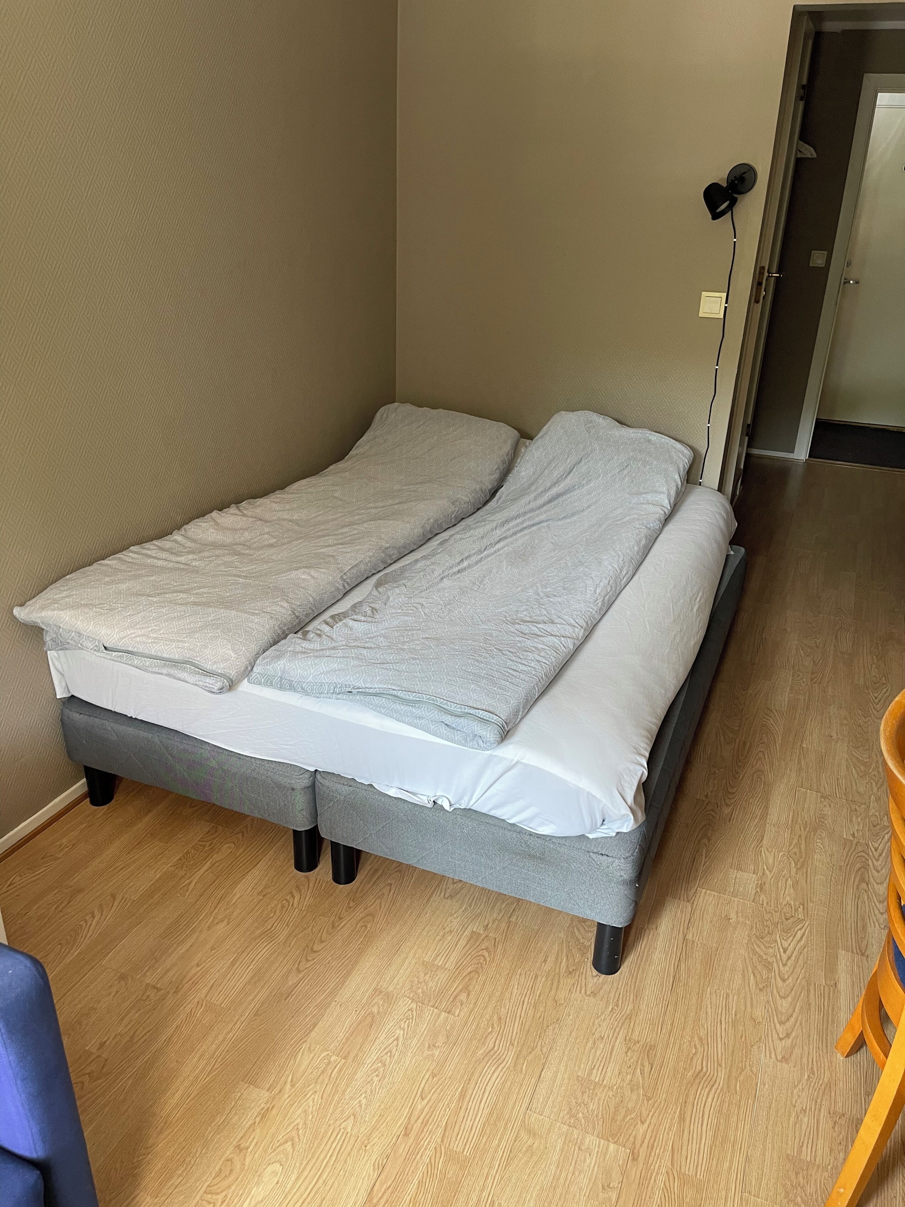 Ein Einzelbett mit grauem Gestell, einer grauen Matratze und einem weißen Kissen.