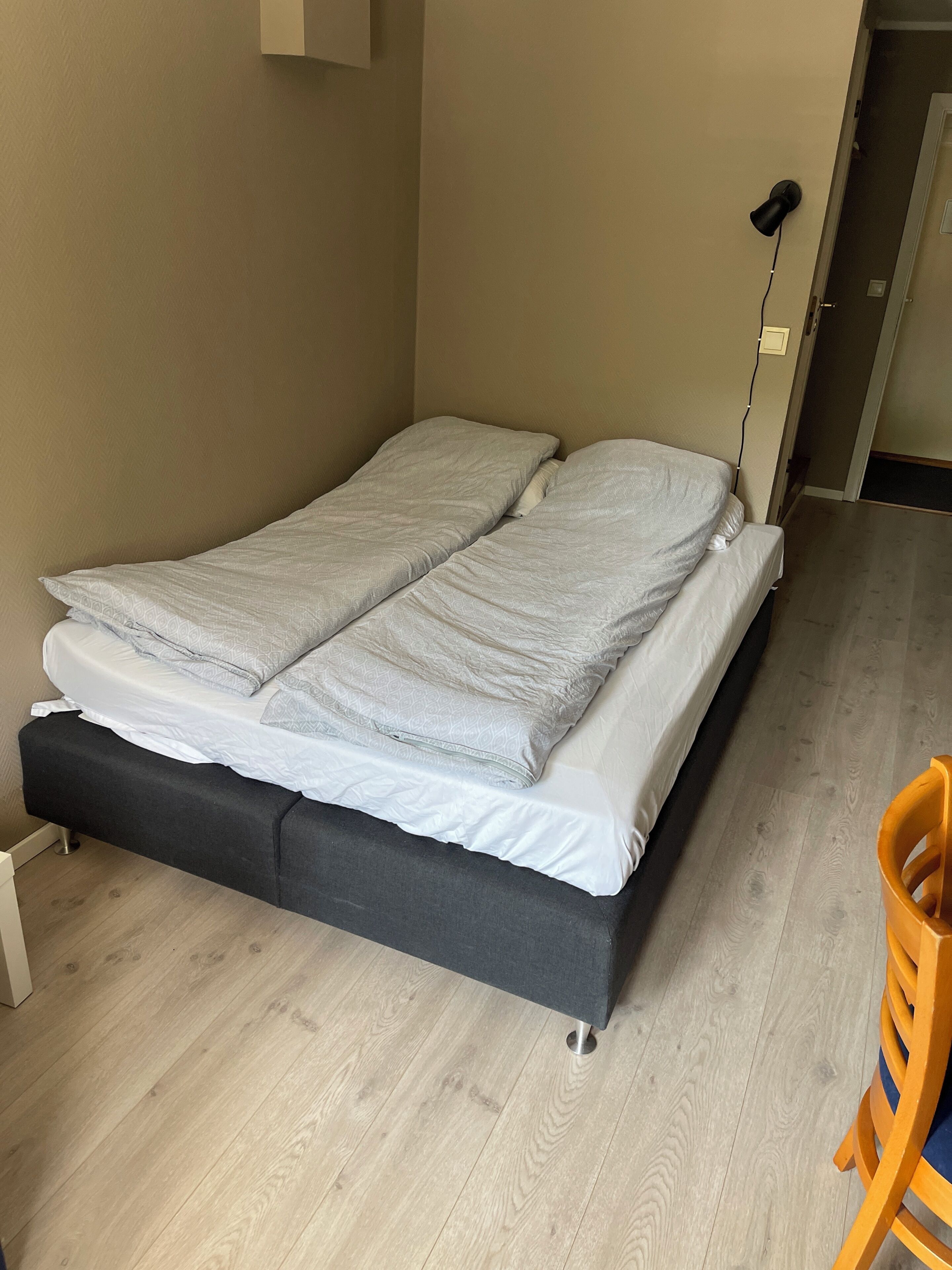 A single bed with a dark frame, a bedside table, and a wooden floor.