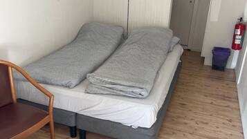 A small, single-bed room with a wooden floor, a chair, a table, and a door leading to another room.