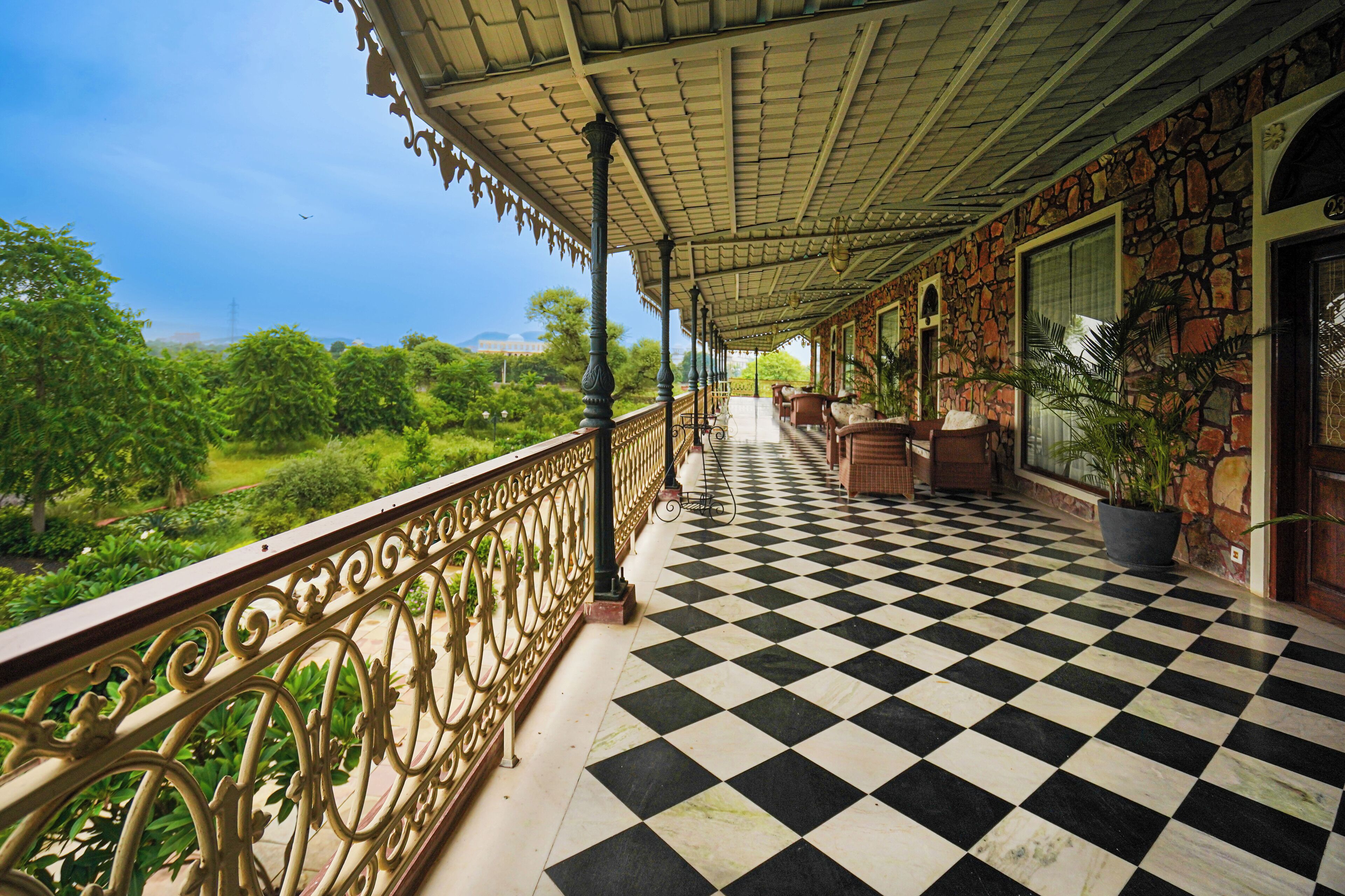 A balcony with a checkered floor, ornate railing, and potted plants.