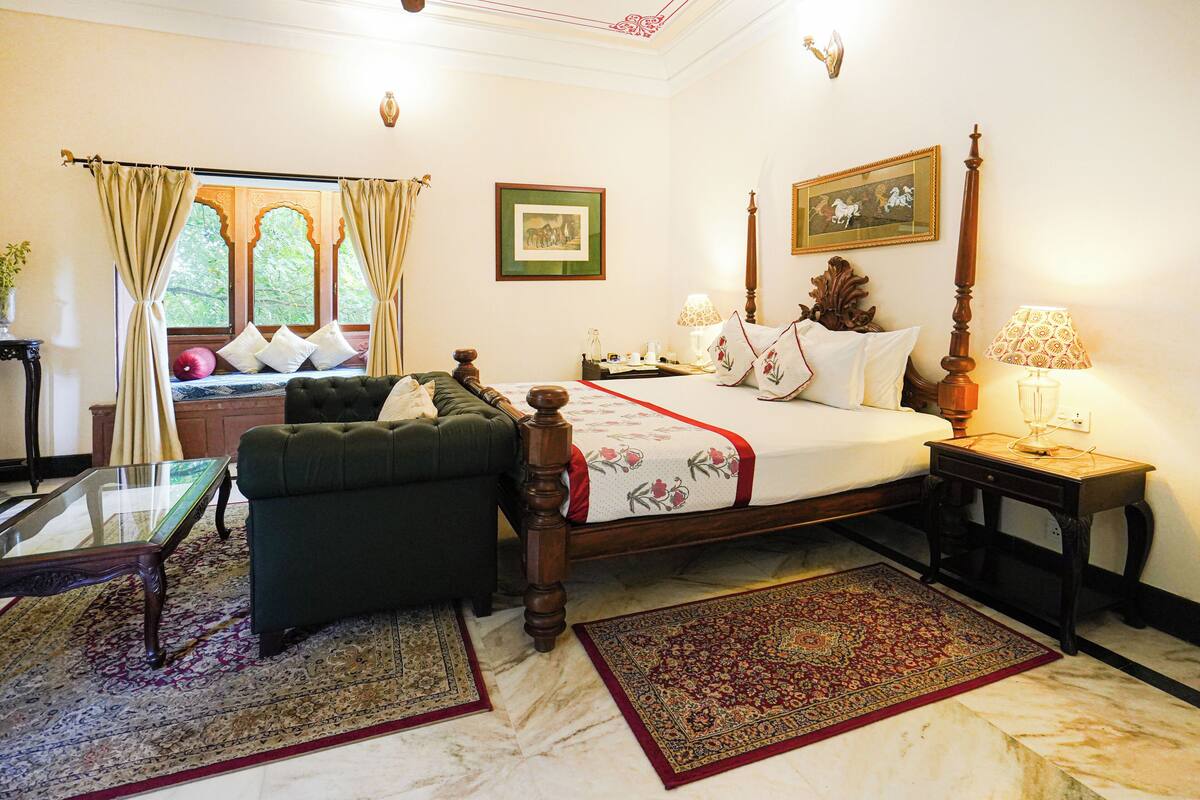 A bedroom with a bed, a green armchair, a nightstand, a lamp, and a window with curtains.