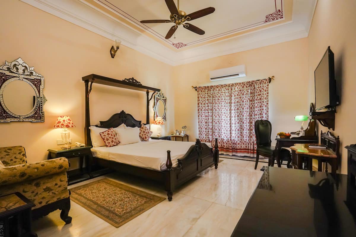 A bedroom with a four-poster bed, a ceiling fan, a large mirror, a desk with a chair, and a television.