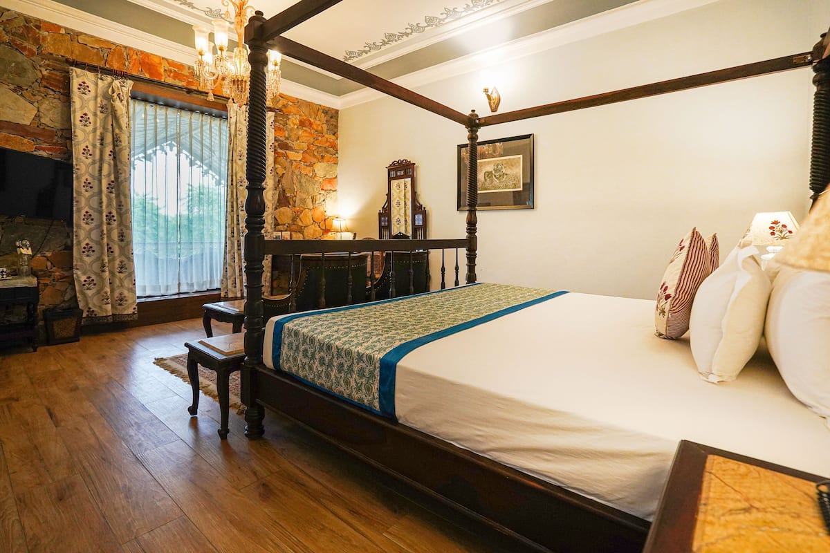 A four-poster bed with a wooden frame, a stone wall, and a chandelier.