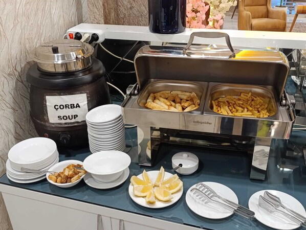 Montaje de bufé con dispensador de sopa de pan de maíz, ensaladera y fuente de fruta.