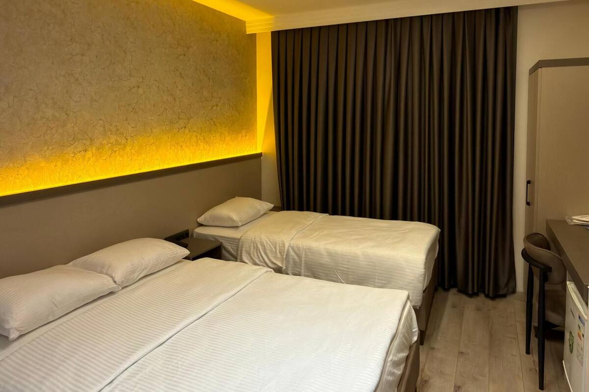 A hotel room with two beds, a desk, a chair, and a curtain.