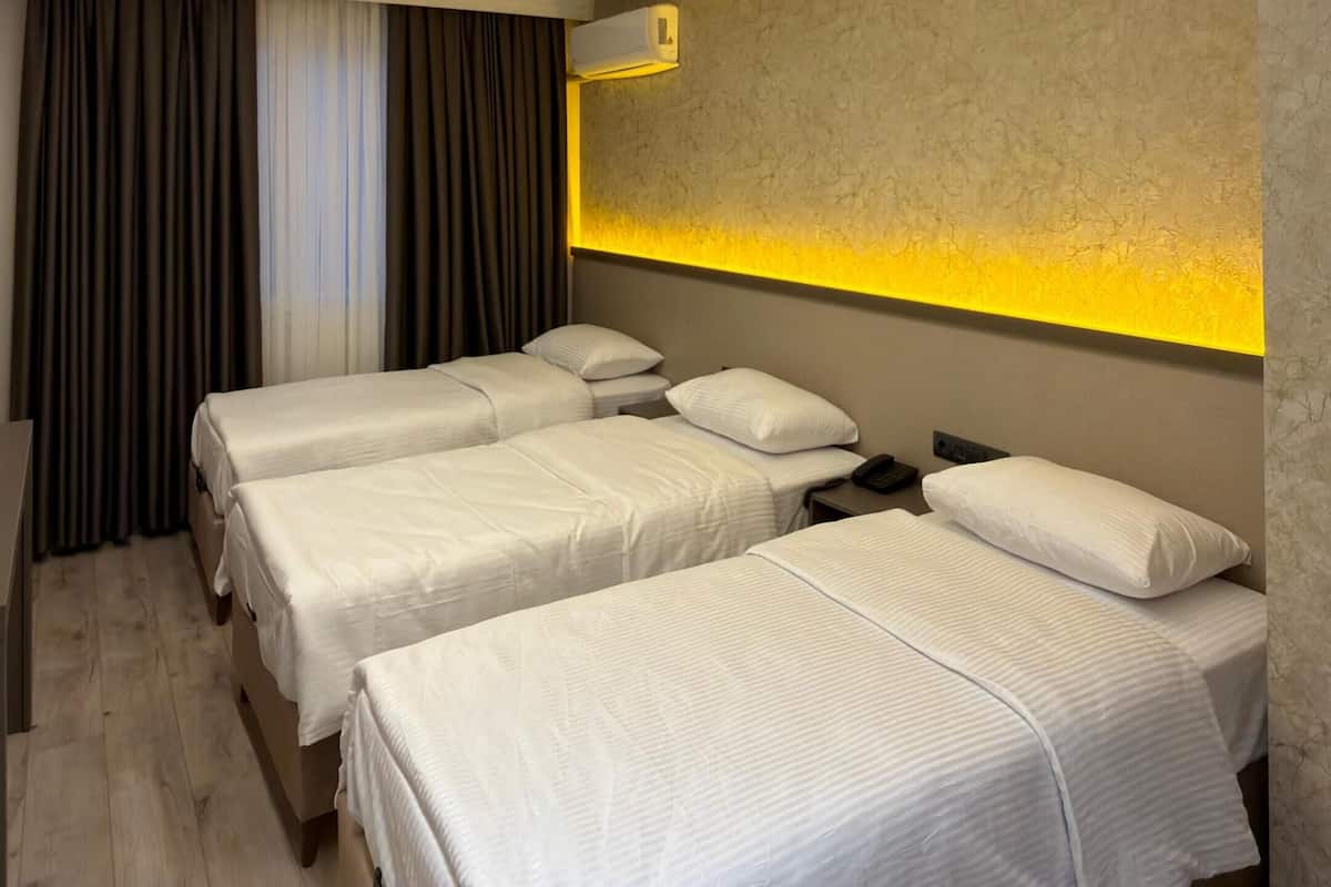 A hotel room with three beds, a wall-mounted air conditioner, and a wooden floor.