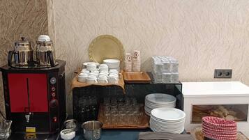 A buffet setup with a coffee machine, plates, glasses, and cutlery.