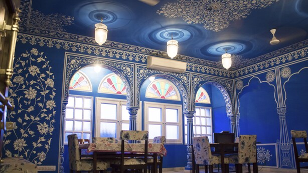 Uma sala de jantar com paredes azuis, padrões florais e janelas em arco.
