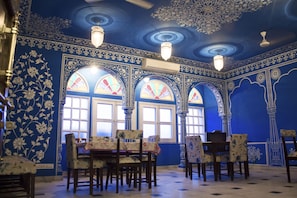 Un espace repas aux murs bleus, orné de motifs floraux et doté de fenêtres en arc de cercle.