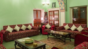 Uma sala de estar com dois sofás vermelhos estampados, uma mesa de centro de madeira e um abajur tradicional.
