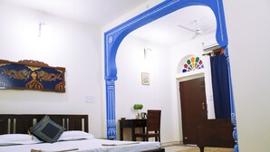 Quarto com uma cama, uma escrivaninha e uma cadeira. Há um arco azul e uma porta com design colorido.