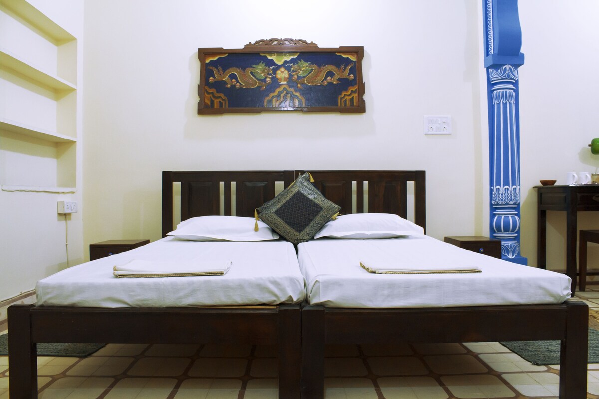 A double bed with white linens and a decorative pillow, a wooden headboard, and a wall-mounted artwork above.