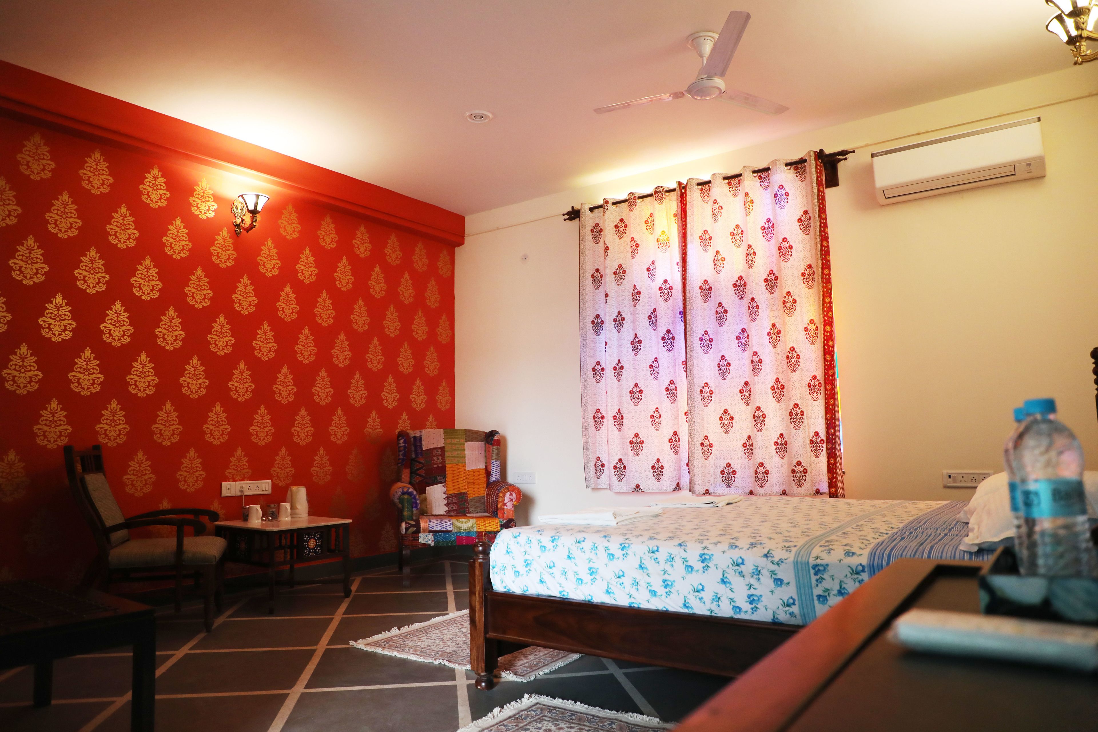 A room with a bed, a chair, a table, and a wall with a patterned wallpaper.