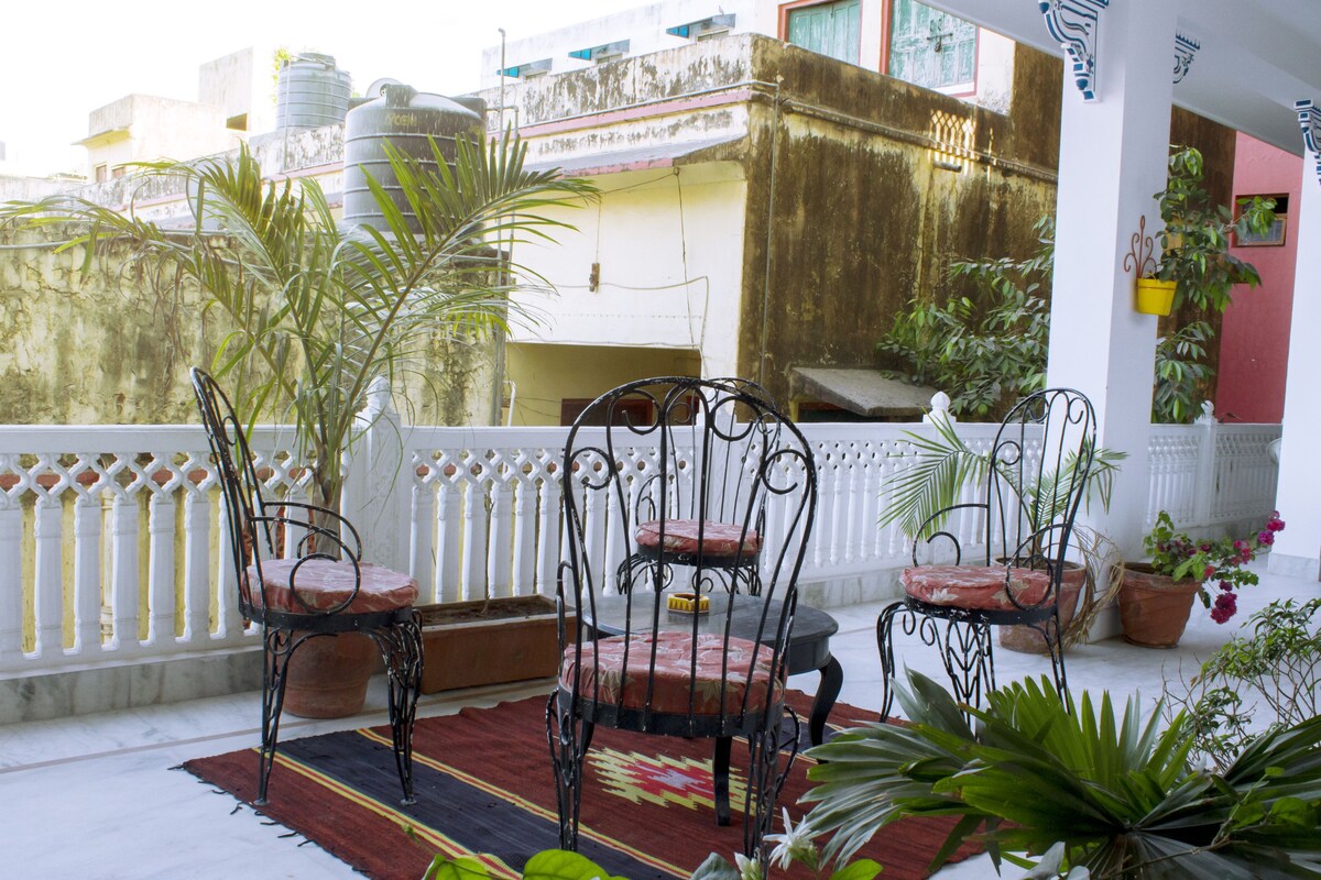 A balcony with two metal chairs, a red and black patterned rug, and potted plants.