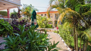 A paved pathway leading to a building with a balcony, surrounded by lush greenery and palm trees. - Romalo Hotel & Apartments (Kigali)