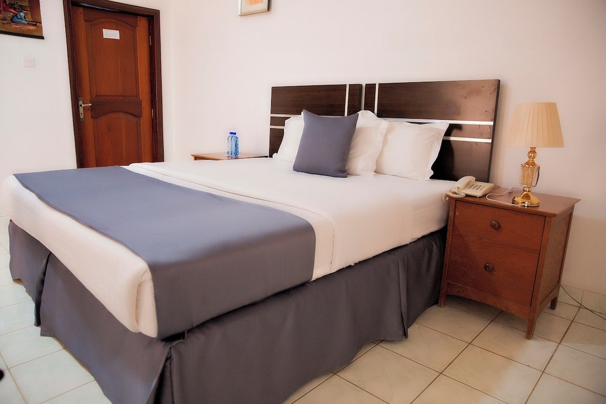 A neatly made bed with a wooden headboard, a bedside table with a lamp, and a water bottle on the nightstand.