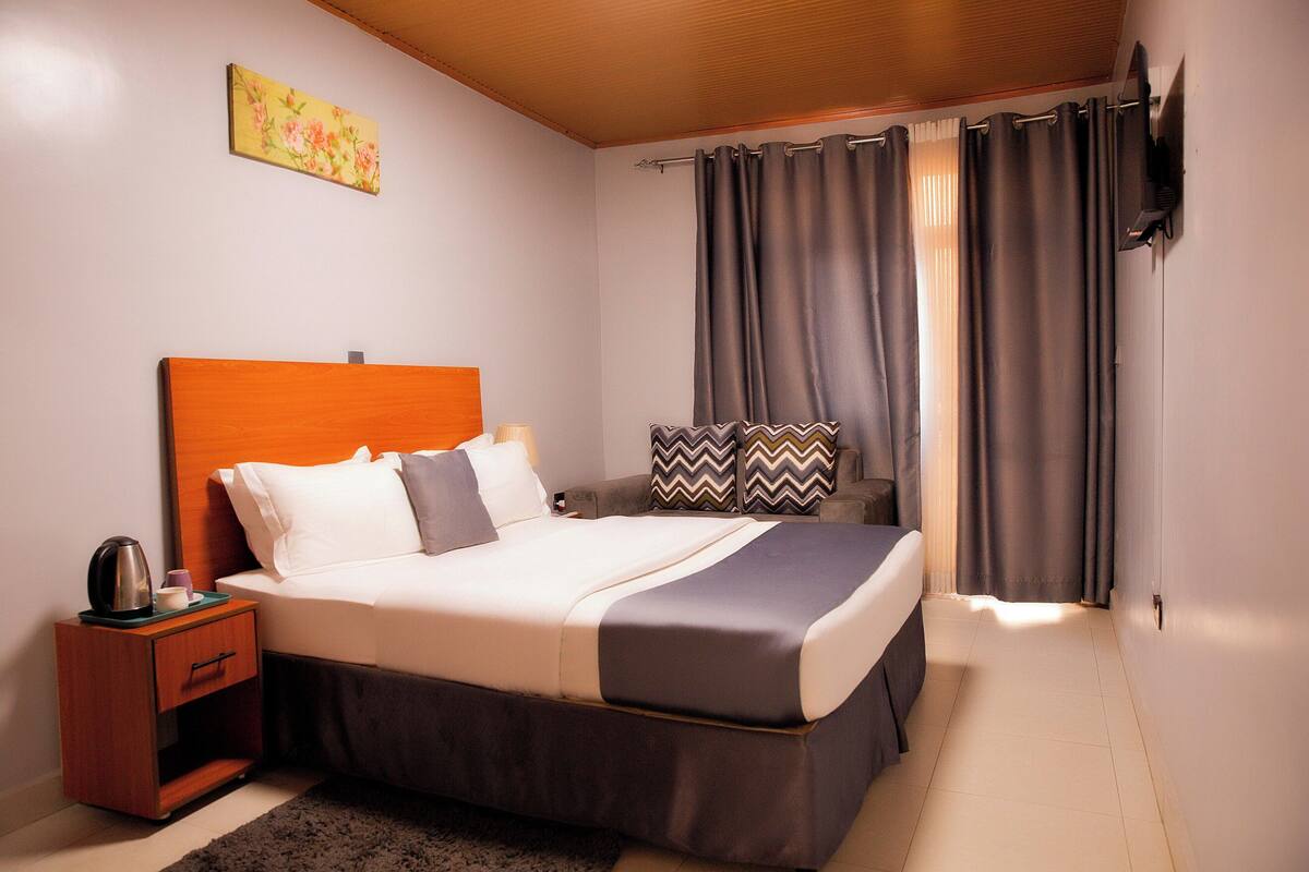 A neatly made bed with a headboard, a bedside table with a lamp, and a wall-mounted TV.
