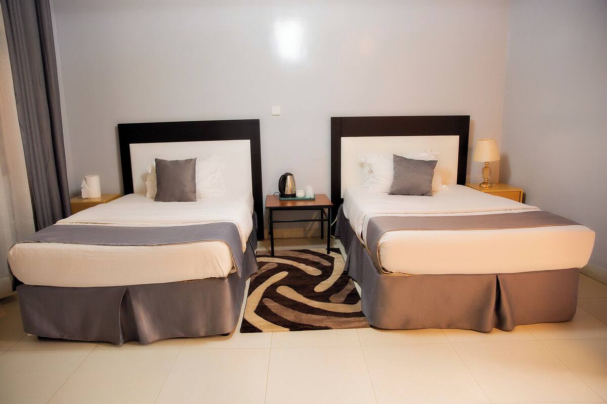 A hotel room with two beds, a small table, and a nightstand with a lamp.