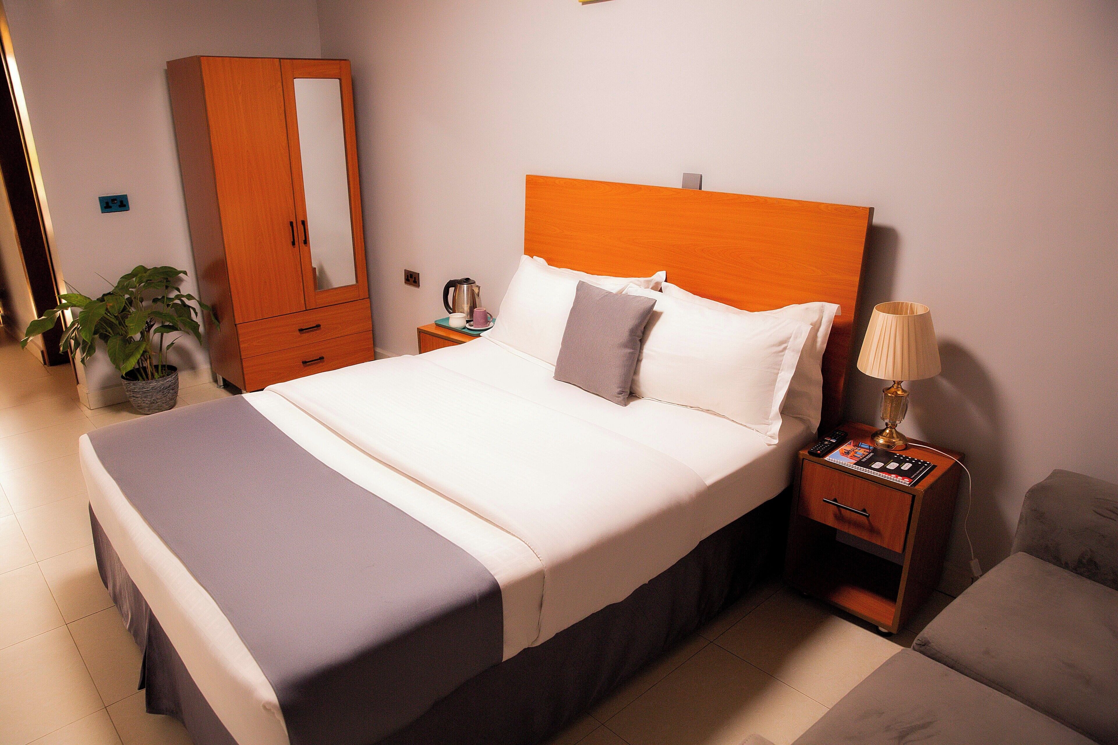 A neatly made bed with a wooden headboard, a bedside table with a lamp, and a wardrobe.