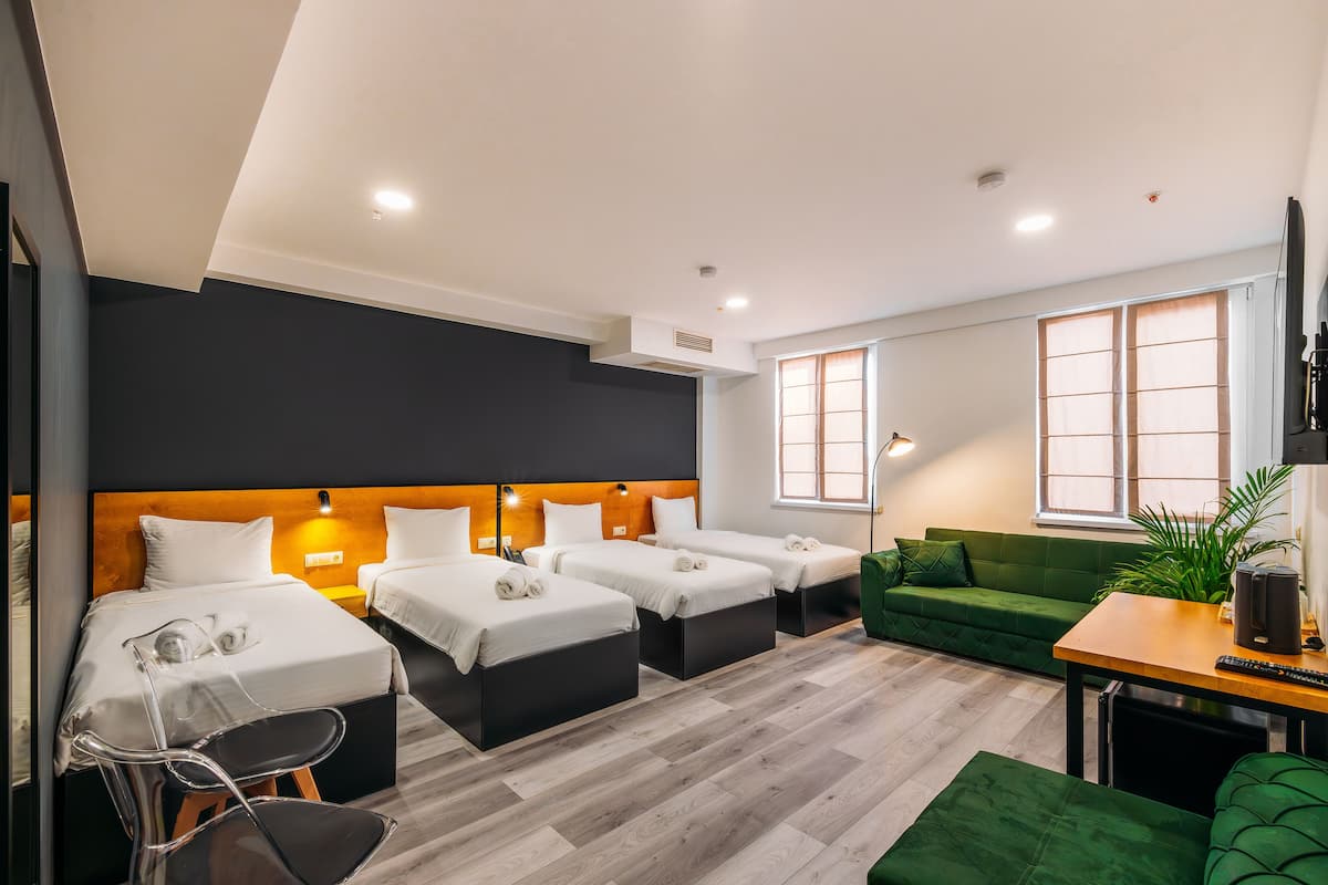 A hotel room with three beds, a green sofa, a small table, and a plant.