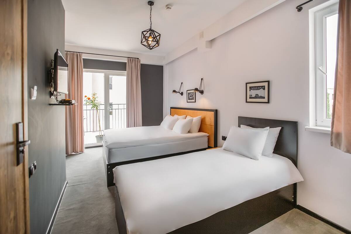 A hotel room with two beds, a large window, a hanging light fixture, and a view of the outdoors.