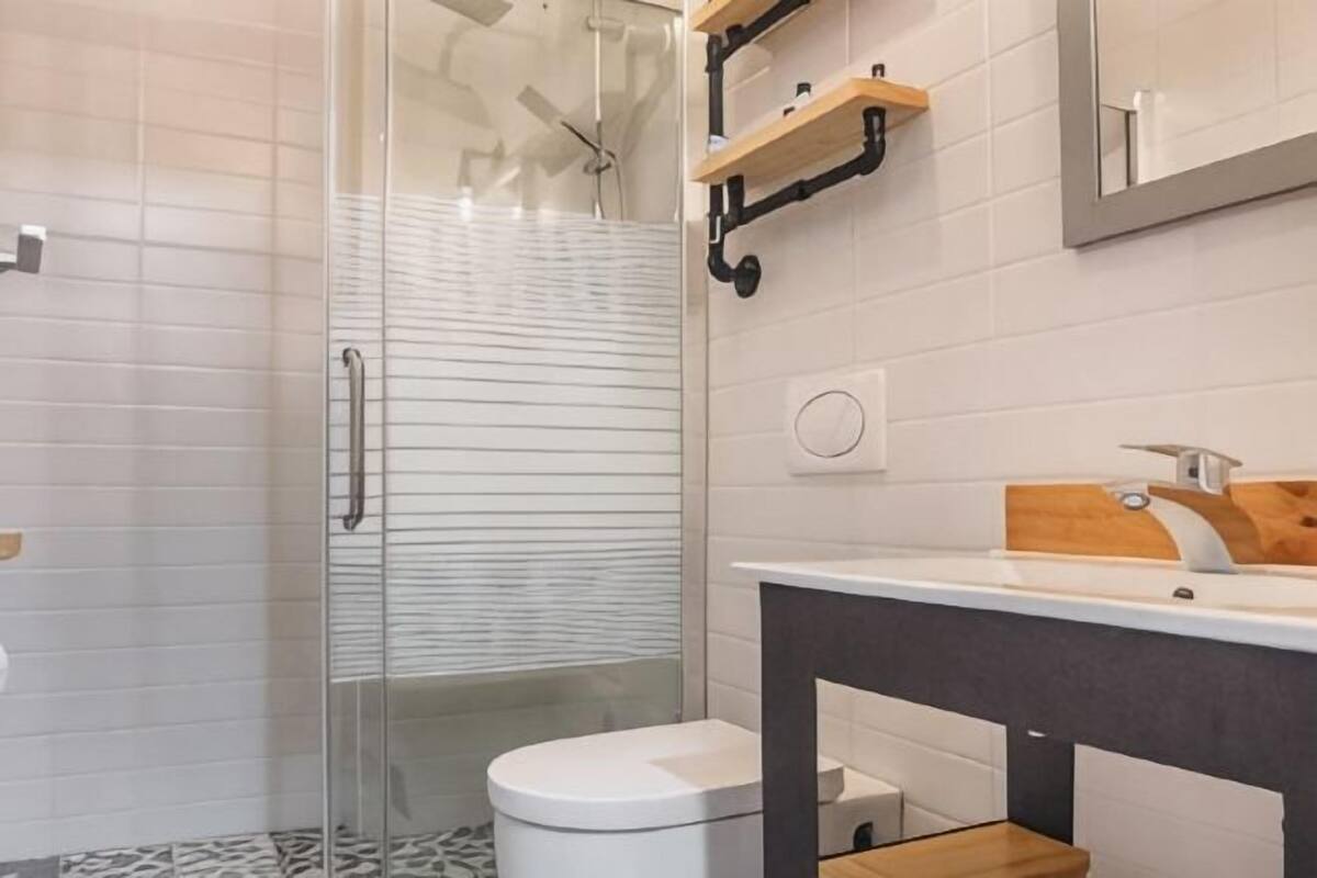 A modern bathroom with a glass shower enclosure, a white toilet, a wooden vanity with a sink, and a mirror above the vanity.