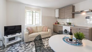 A modern living room with a flat-screen TV, a beige sofa, a glass dining table, and a kitchen with a washing machine. - Buonarroti (Florence)