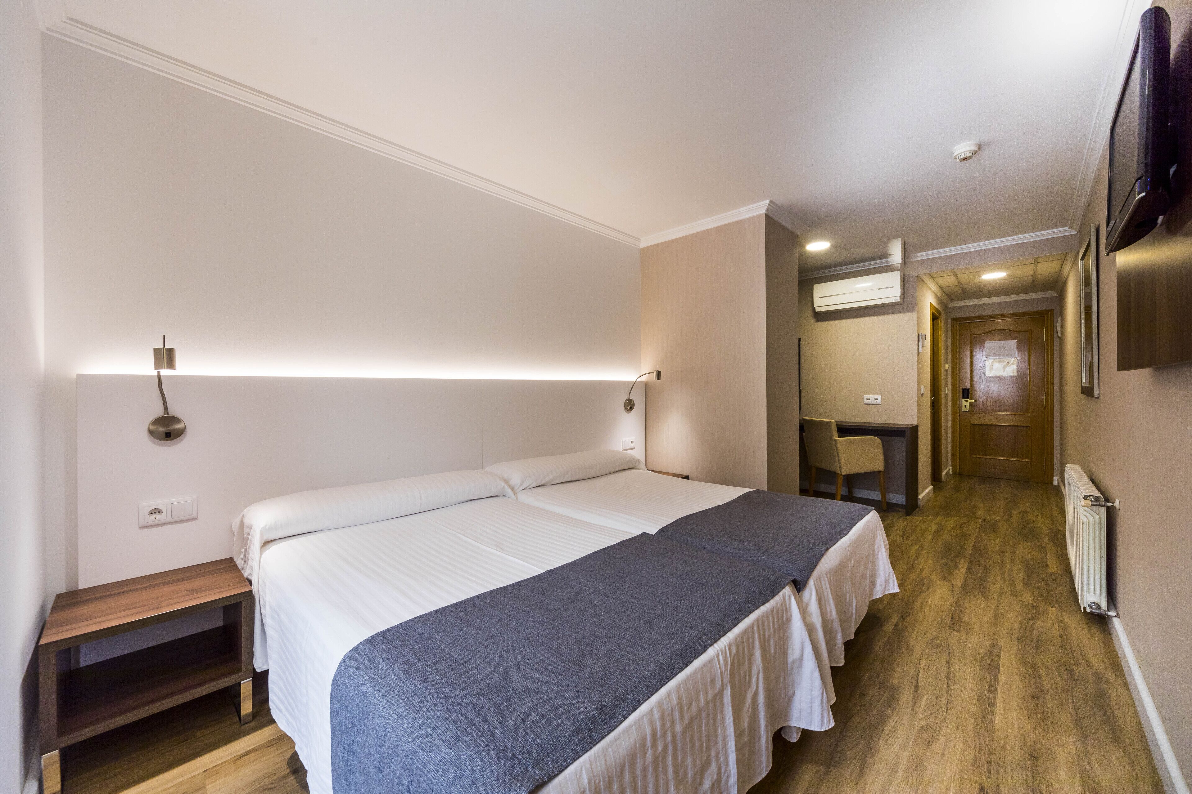 Una habitación de hotel con una cama grande, mesitas de noche, un escritorio y una silla.