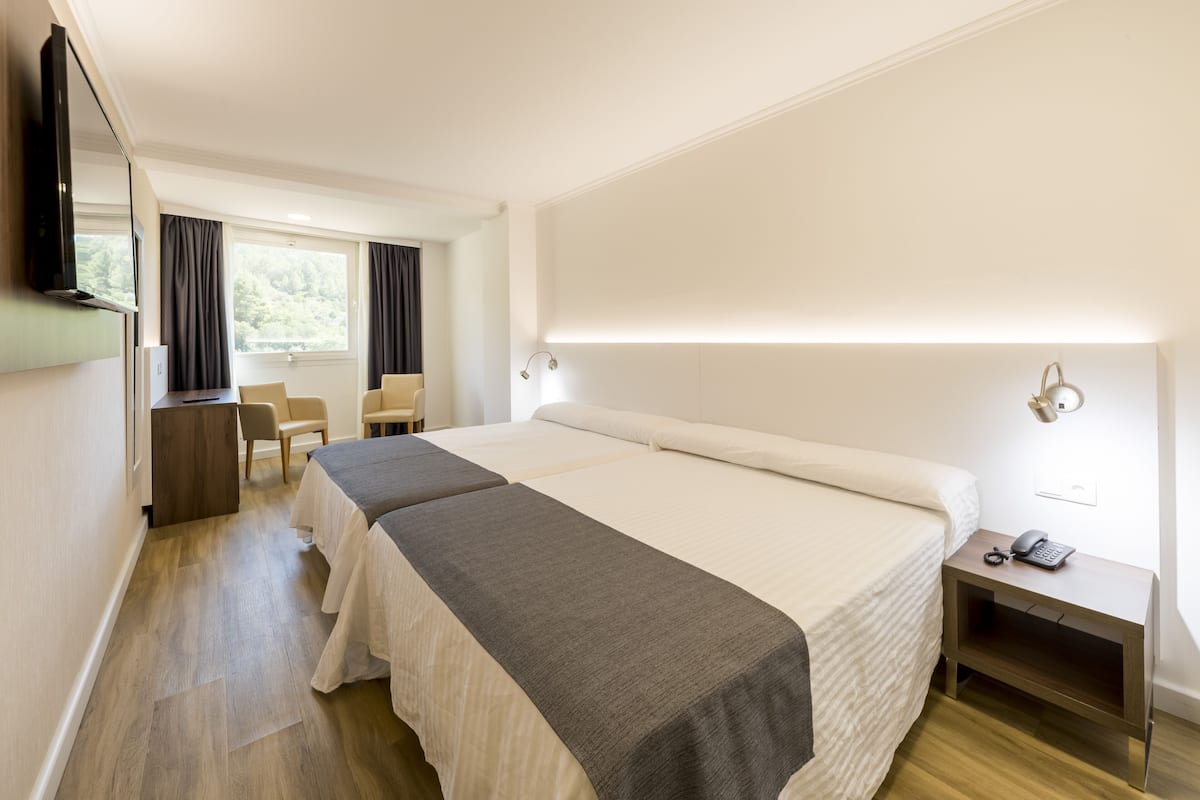 A hotel room with two beds, a desk, a chair, a TV, and a bedside table with a phone.