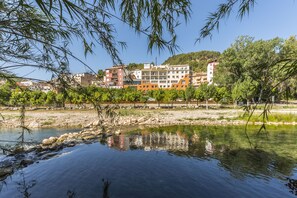 A riverside view with a building complex in the background. - Rosaleda Del Mijares (Montanejos)